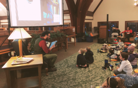 Adrian reading stories to seated children in front of the big screen with the pages projected.