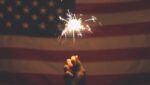Hand holding a sparkler in front of an American flag