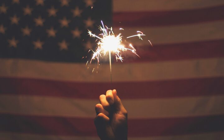 Hand holding a sparkler in front of an American flag