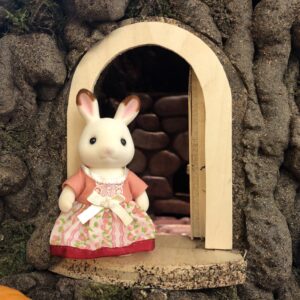 Rabbit in red dress in from of door to home in hollow of tree