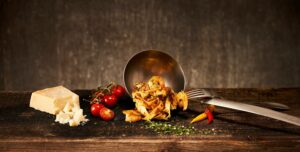a board with cheese, tomatoes, and a ladle of pasta